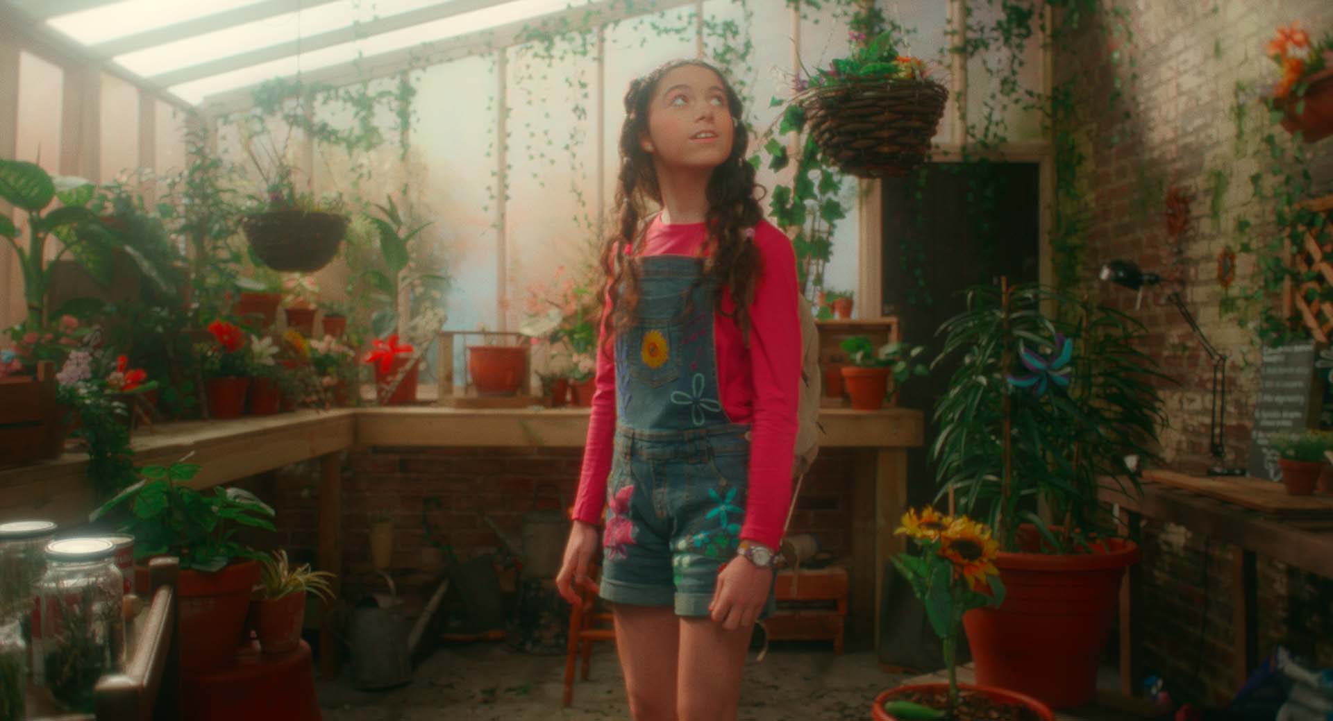 Girl stood in a greenhouse surrounded by plants.